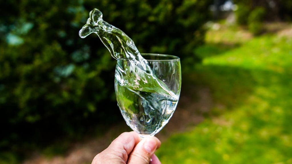 Water splashing out of a wineglass in natural light outdoors, symbolizing healthy daily habits.