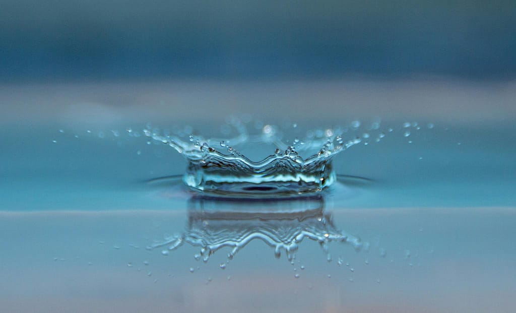 Macro shot of a water droplet creating a ripple effect on the water surface.