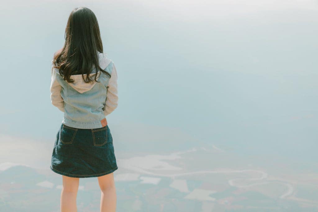 Back view of a young girl in a denim jacket gazing at a vast scenic landscape, capturing a sense of freedom and Personal Growth.