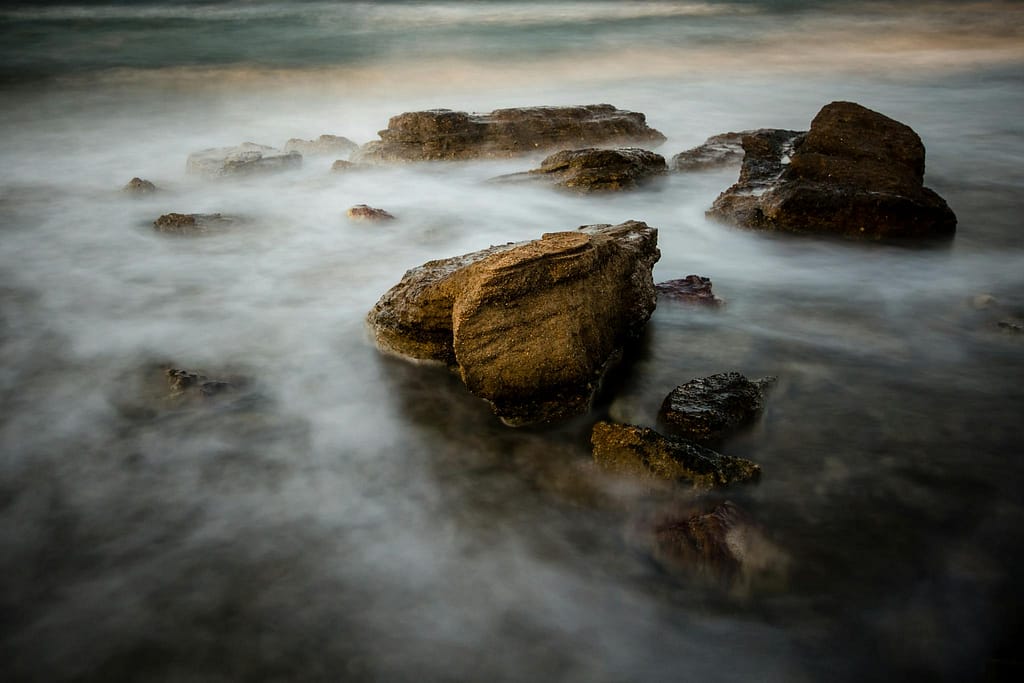Serene coastal scene with rocks and misty ocean water, evoking tranquility.