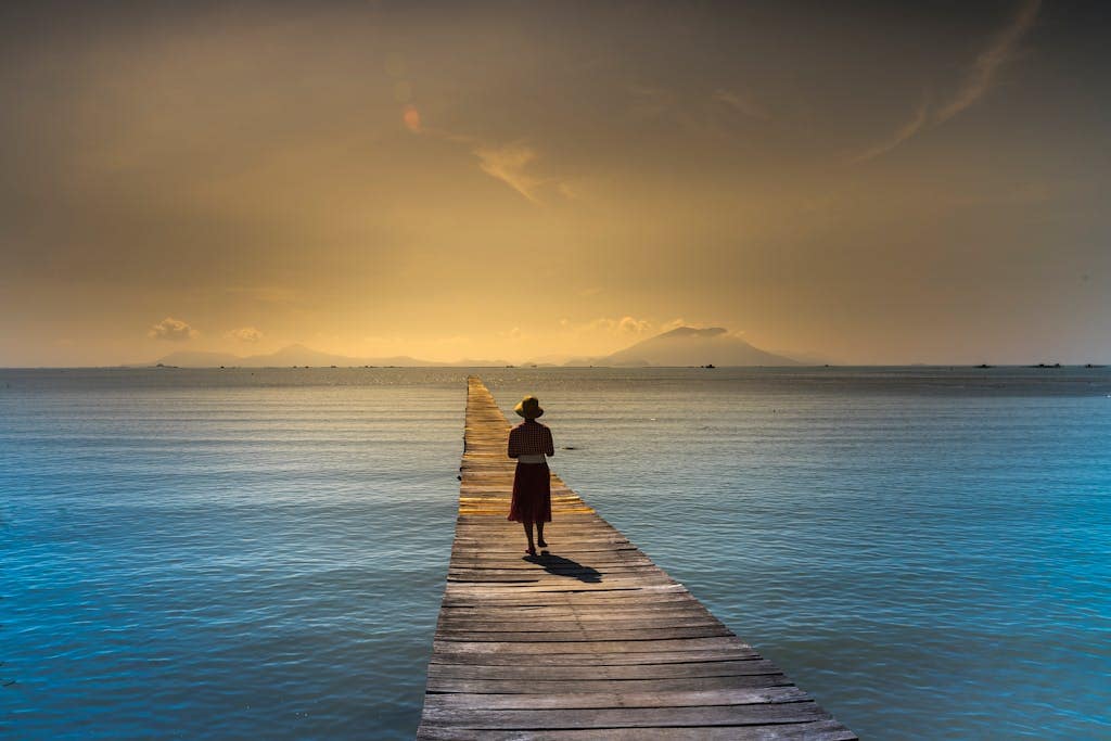 Woman walks along a wooden pier at sunrise with calm ocean waters surrounding her symbolizing a fresh start in life.