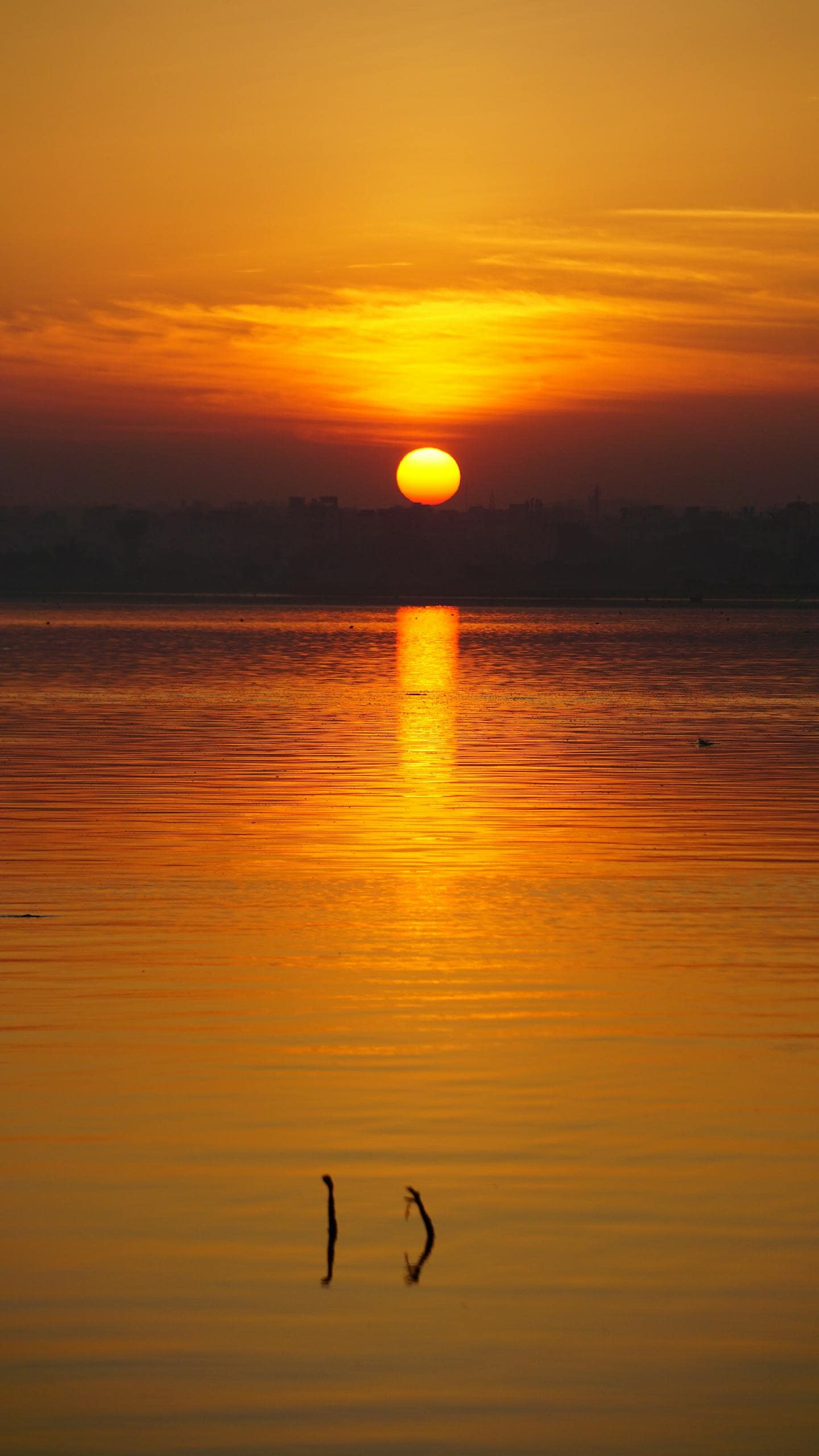 Beautiful sunrise over a calm lake with vibrant orange hues and sun rays in Hyderabad, India.