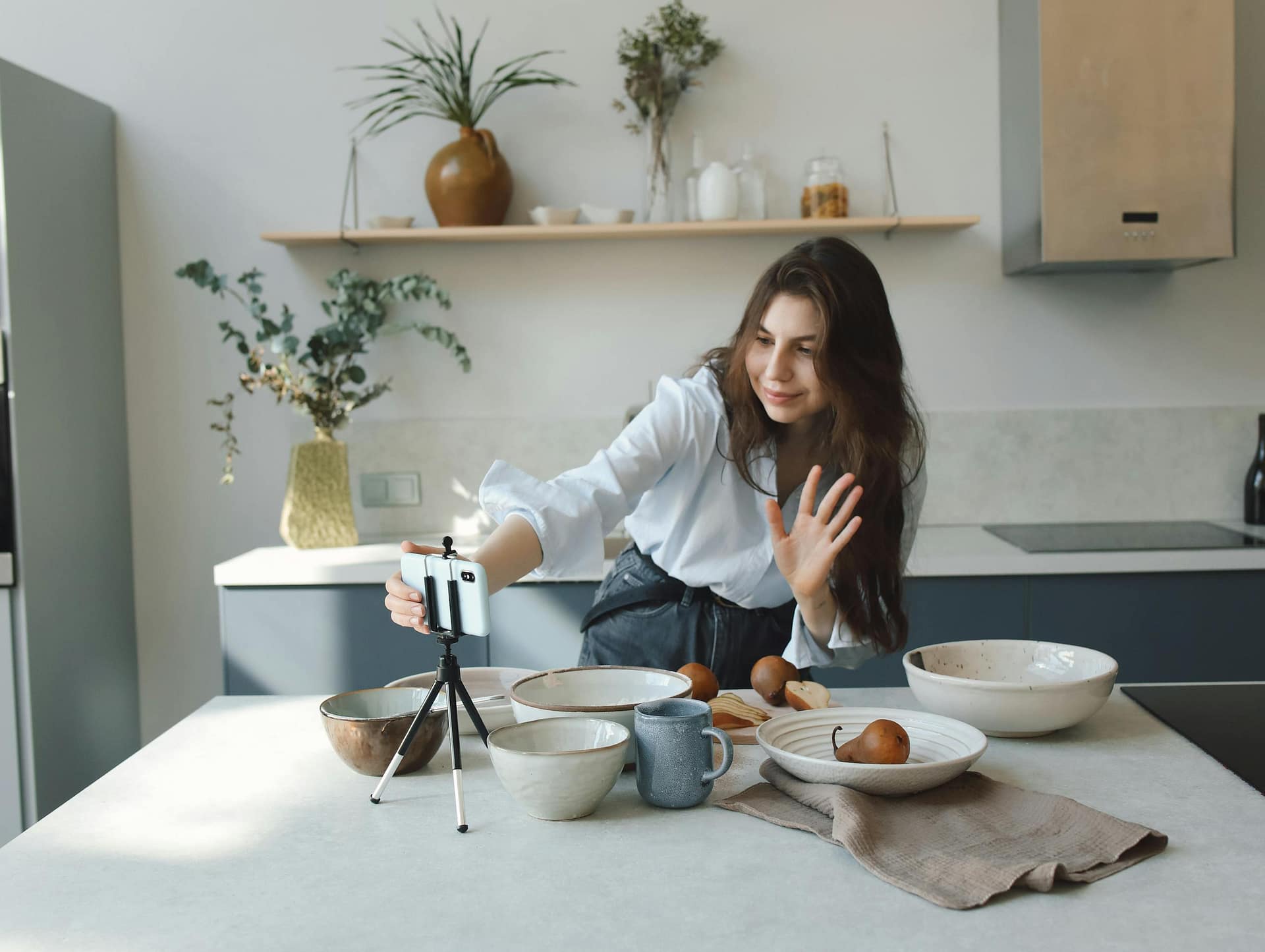 Woman filming cooking video in modern kitchen with smartphone and tripod for social media.