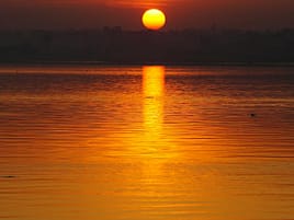 Beautiful sunrise over a calm lake with vibrant orange hues and sun rays in Hyderabad, India.