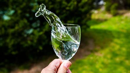 Water splashing out of a wineglass in natural light outdoors, symbolizing healthy daily habits.