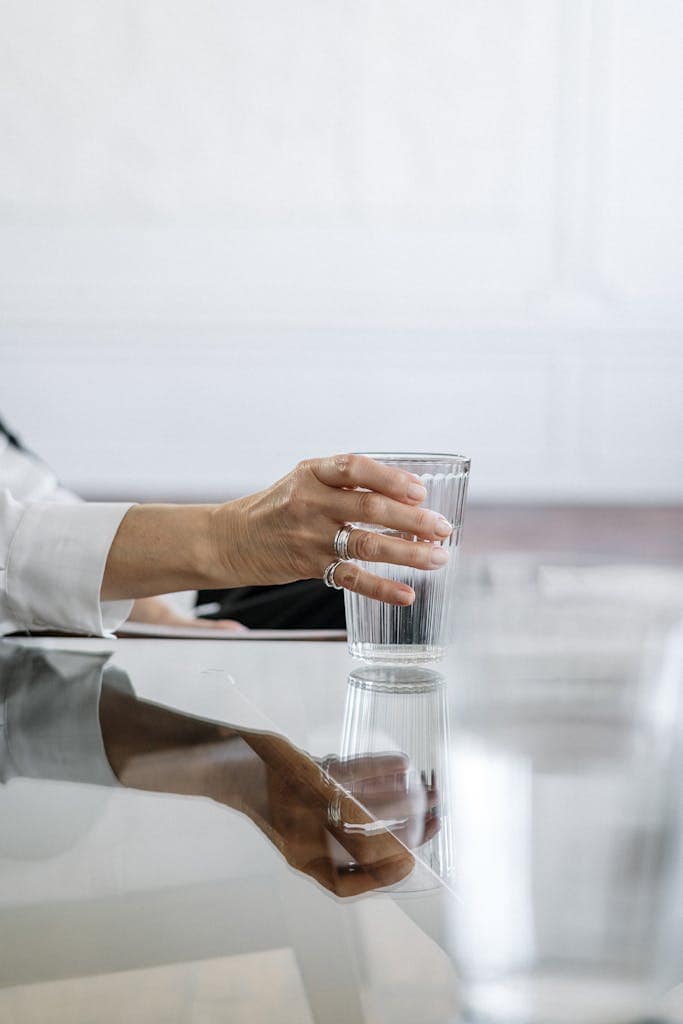 Close-up of a hand with holding a glass of water on a glass table, perfect for everyday well-being.